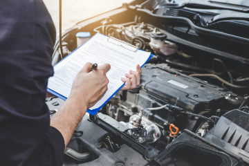 Mechanic inspects car with clipboard to note possible defects.