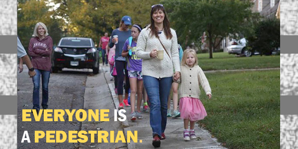 Parents walking on sidewalk with children and text reading "everyone is a pedestrian"