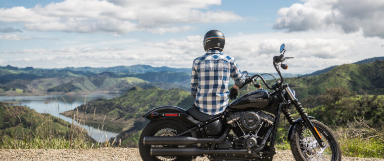 Person with helmet on sitting on motorcycle, facing away from camera looking over mountain range.