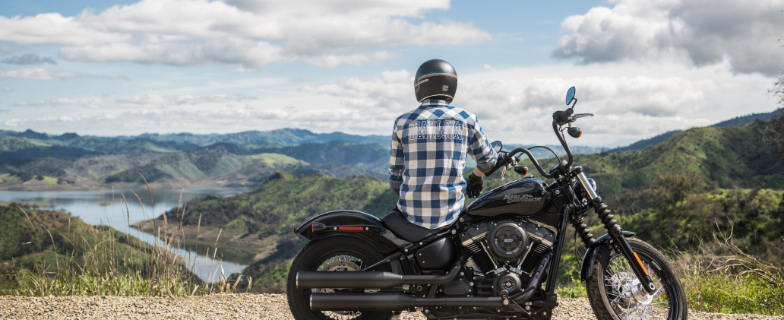 Person with helmet on sitting on motorcycle, facing away from camera looking over mountain range.