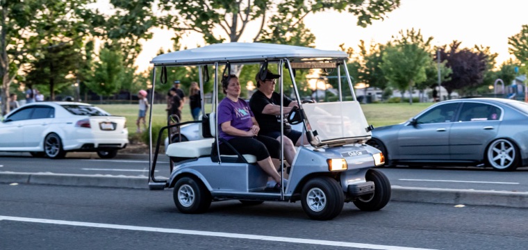 Two people driving a golf cart down a public street