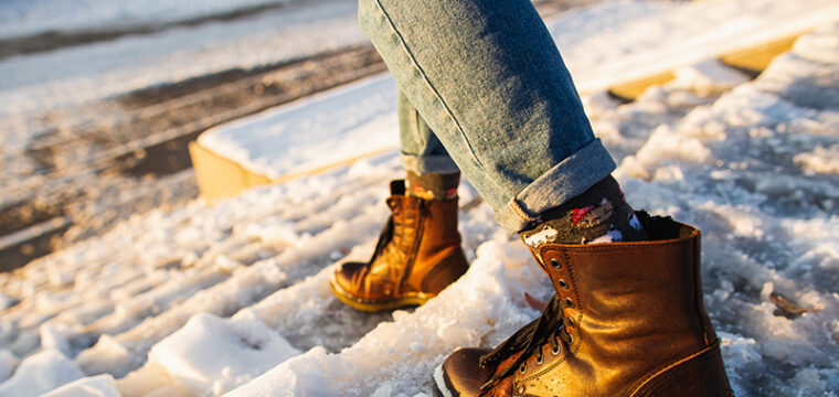 A person wearing jeans and boots walks on snowy steps, at risk for winter weather injuries