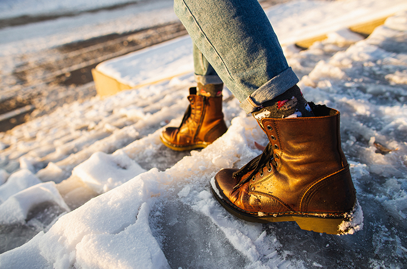 A person wearing jeans and boots walks on snowy steps, at risk for winter weather injuries