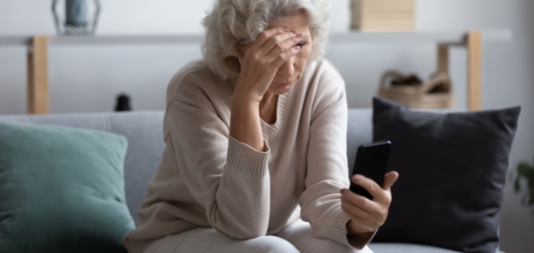 A senior woman sits on her couch and looks at her phone due to phone holiday scams