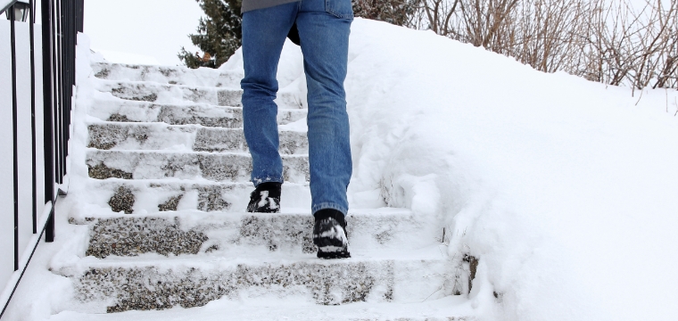 Man wearing blue jeans risks a slip and fall walking on icy stairs