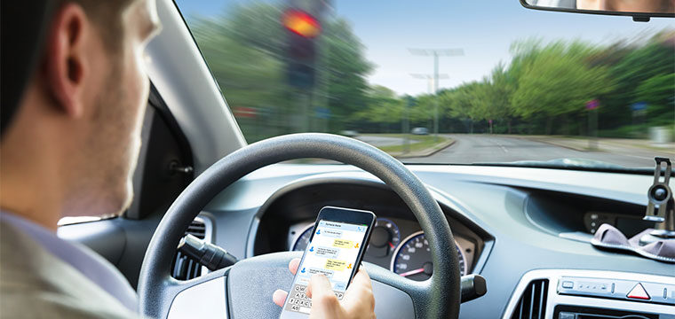 A middle aged man on his phone in the driver seat of a car, one of the primary causes of distracted driving.
