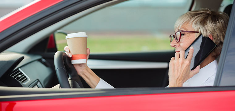 A woman holds a coffee and engages in texting while driving.