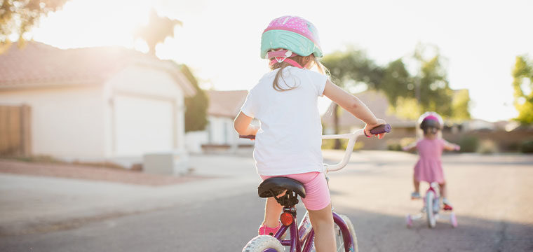 Two young children ride bikes in a neighborhood street, practicing bike safety by wearing helmets