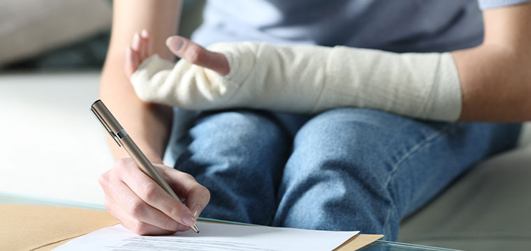 A person wearing a cast fills out paperwork for their personal injury claim.
