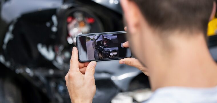man taking picture of car damage on his phone after a hit-and-run auto collision