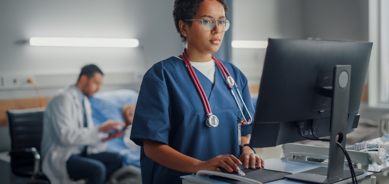 Nurse reviewing labs while doctor sits with patient in the background